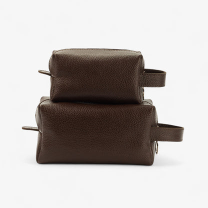 Two brown leather toiletry bags stacked on a white background