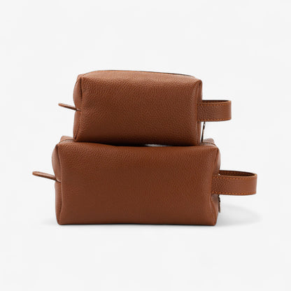 Two brown leather toiletry bags stacked on a white background