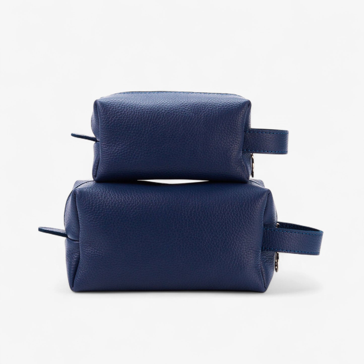 Two navy blue leather toiletry bags stacked on a white background