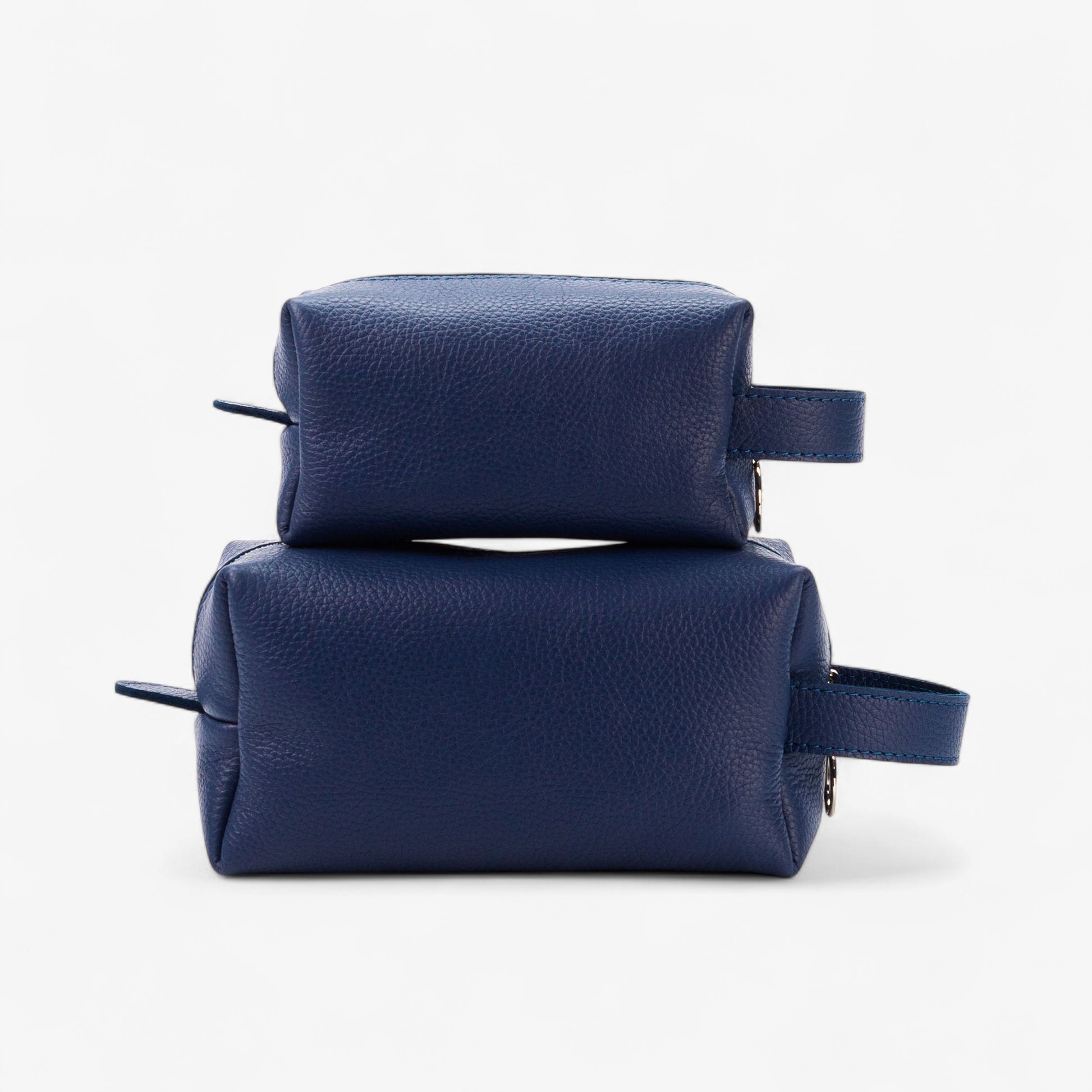 Two navy blue leather toiletry bags stacked on a white background