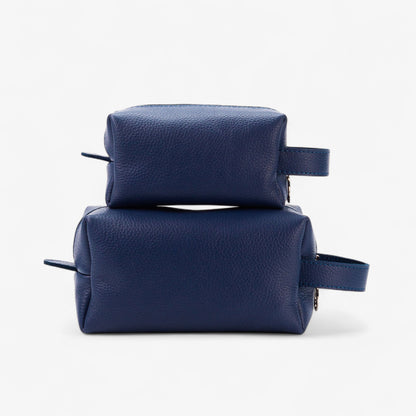 Two navy blue leather toiletry bags stacked on a white background