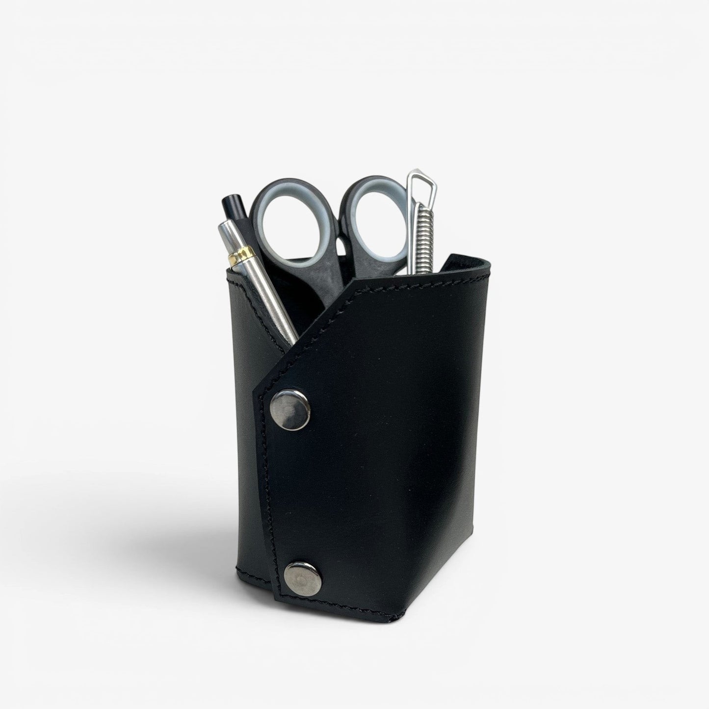 Pache black leather pen and brush holder with silver snap closures, holding pens and scissors on a desk.
