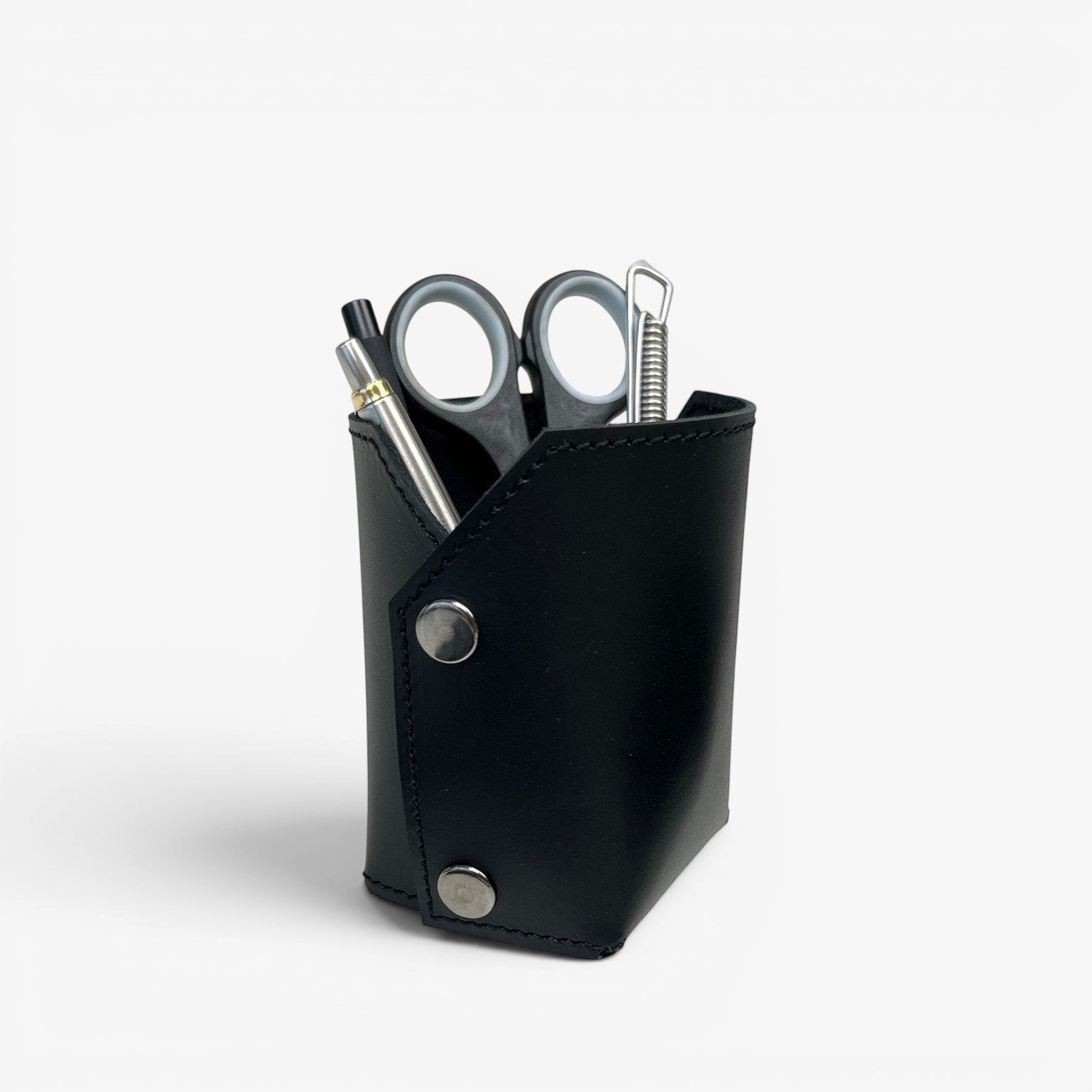 Pache black leather pen and brush holder with silver snap closures, holding pens and scissors on a desk.