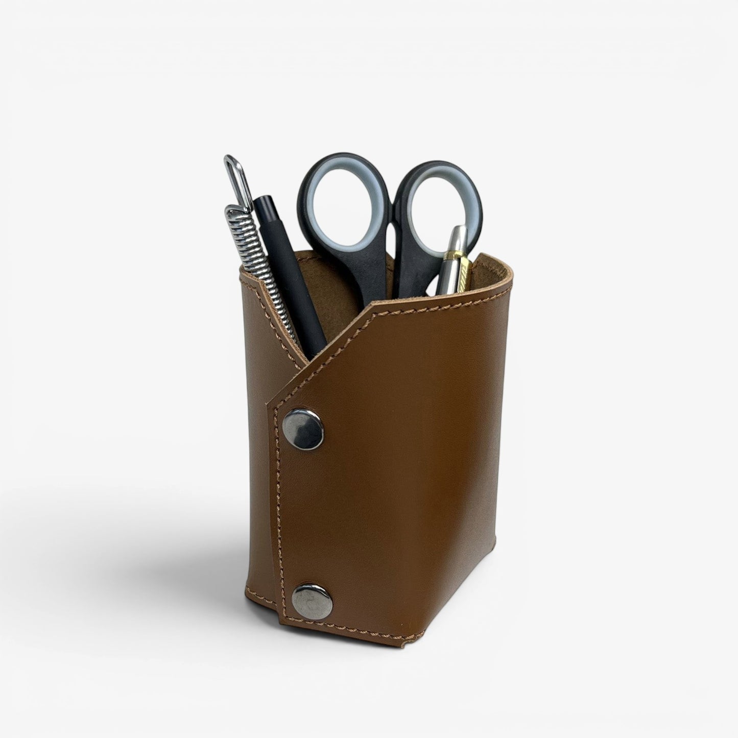 Pache brown leather desk organizer holding pens, scissors, and a plant in a white pot. Minimalist design.