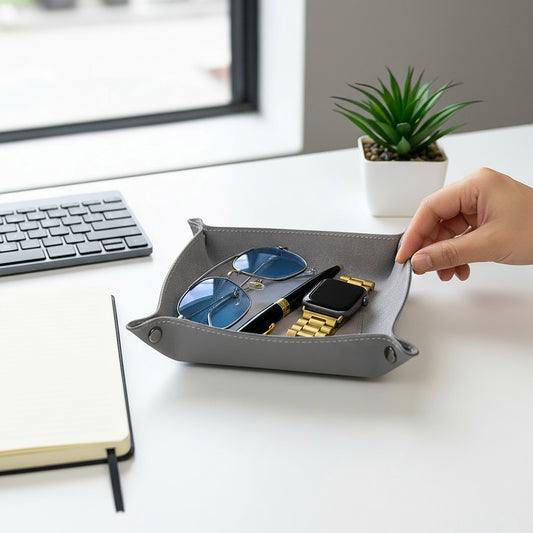 Pache gray leather desk catchall tray holding blue-lens glasses, a black pen, and a gold smartwatch. Minimalist design.