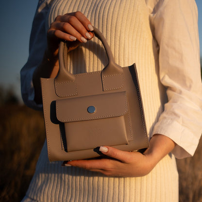 Pache gray smooth leather mini tote bag with front pocket and silver snap closure. Woman holding bag by handles.