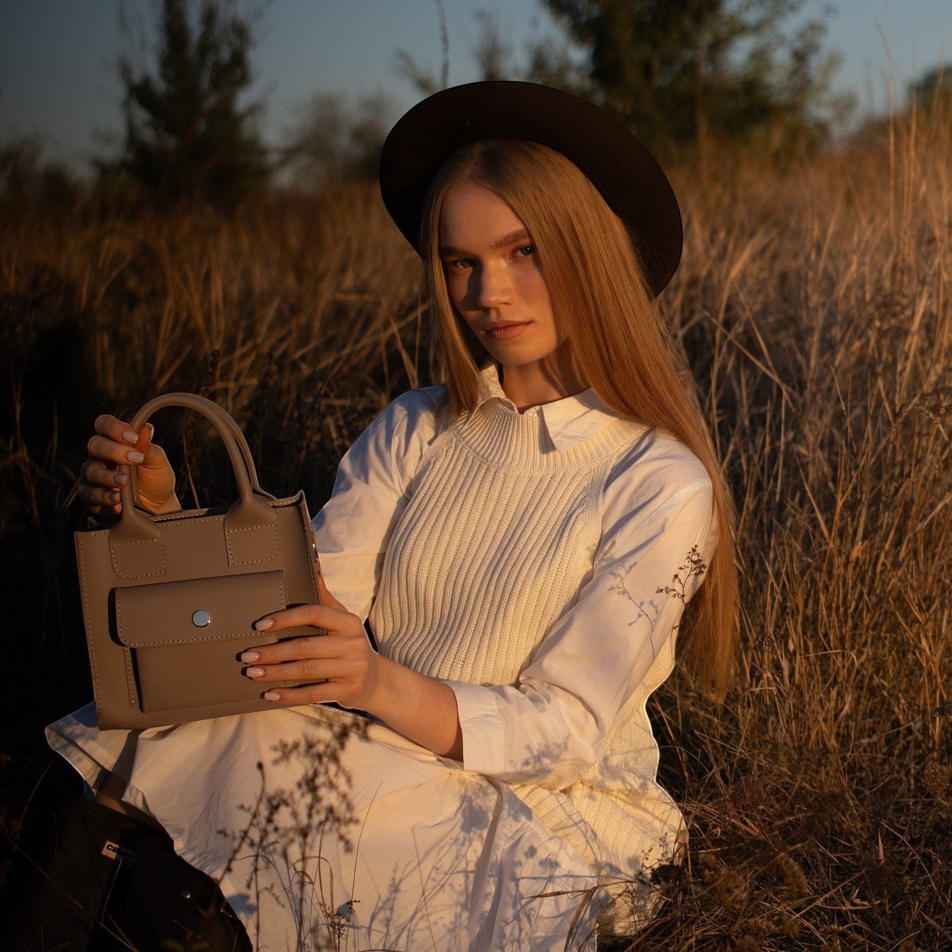 Pache gray smooth leather mini tote bag with a structured shape and front pocket, held by a woman in a field.