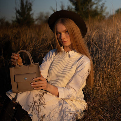 Pache gray smooth leather mini tote bag with a structured shape and front pocket, held by a woman in a field.
