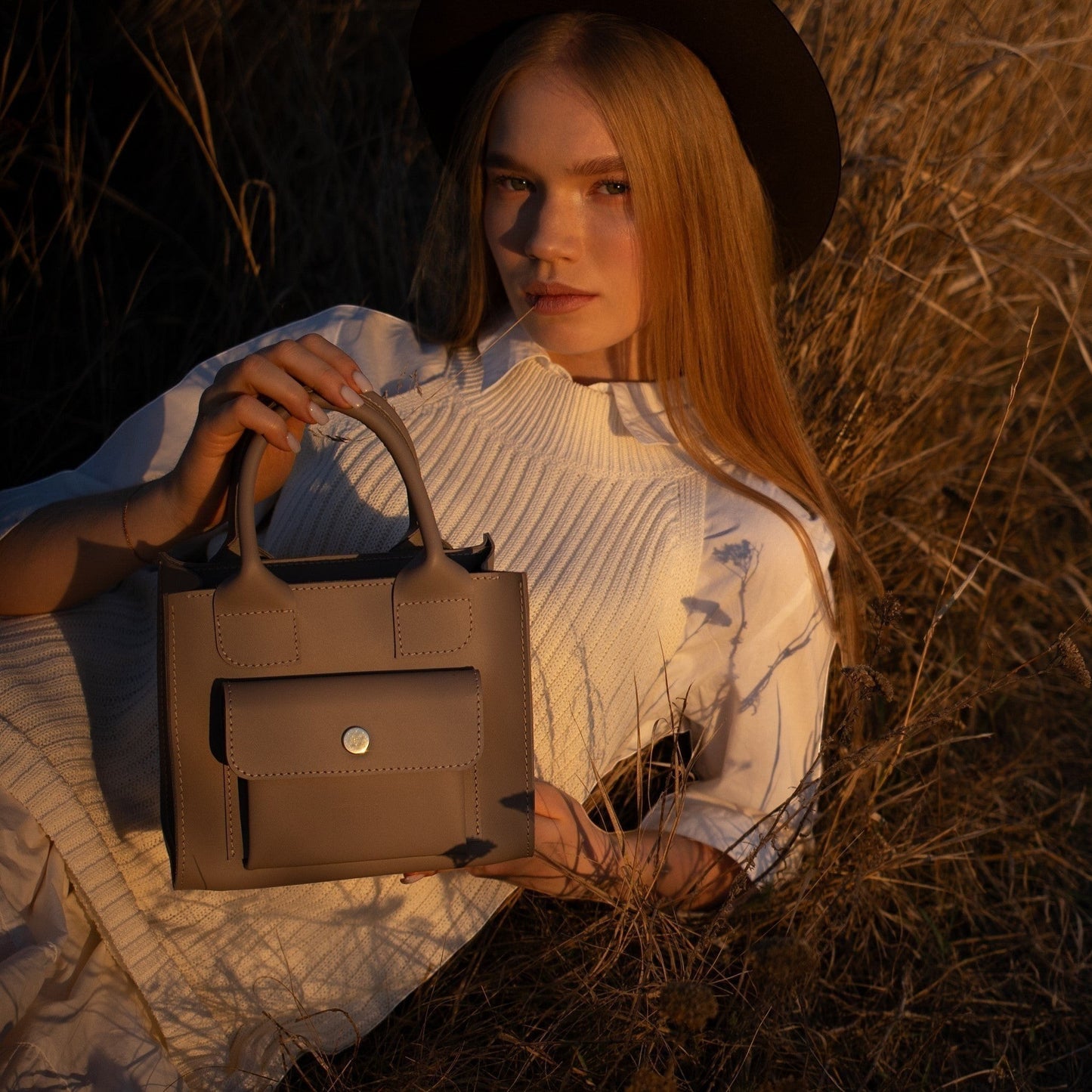 Pache gray mini tote bag made of smooth leather with a structured shape and front pocket. Model holds bag in a natural setting.