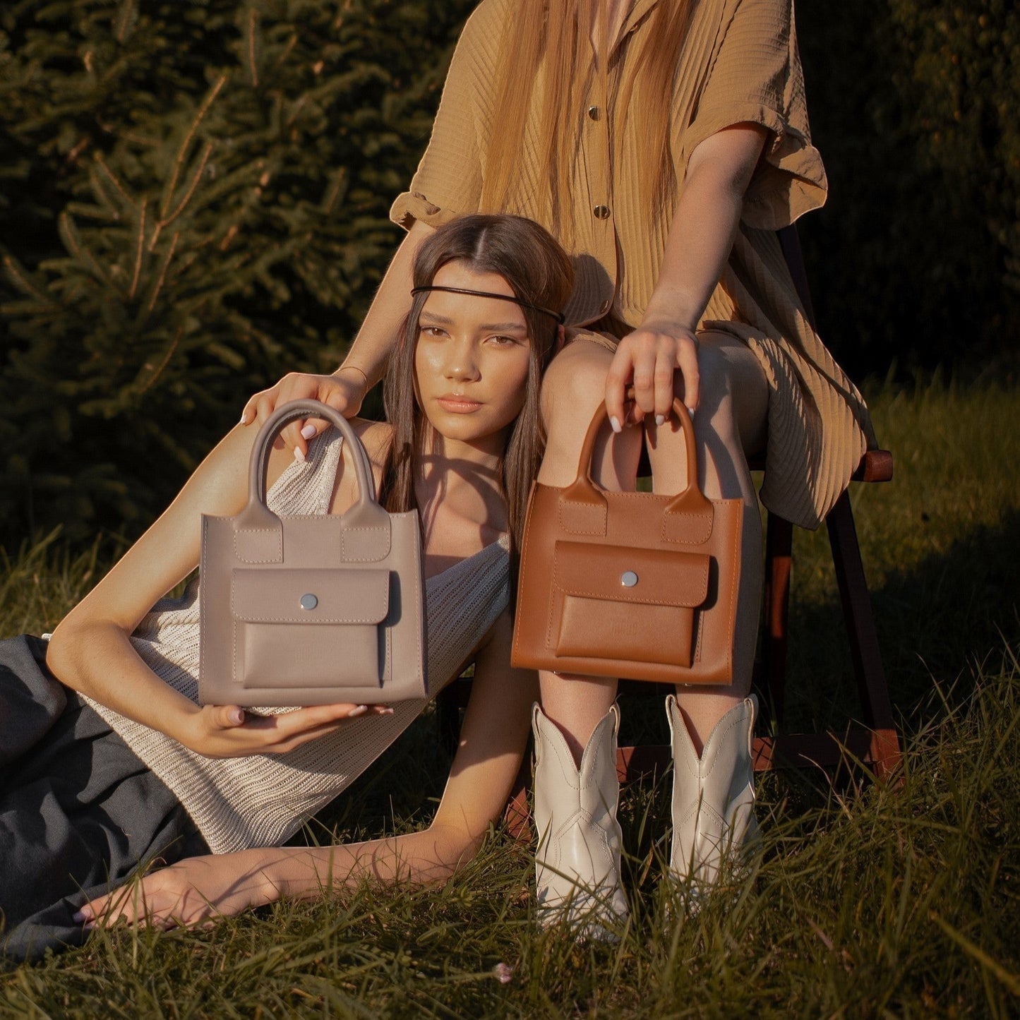 Pache gray mini tote bag made of smooth leather with a front pocket and silver button closure. Two women are holding the bags outdoors.