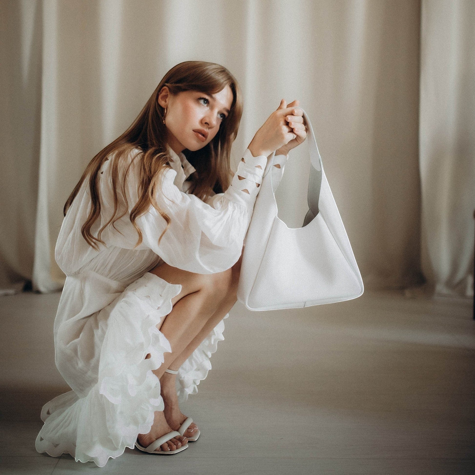 Pache white leather hobo bag with matching wallet, magnetic closure, and unique strap detail. Model wearing white dress.